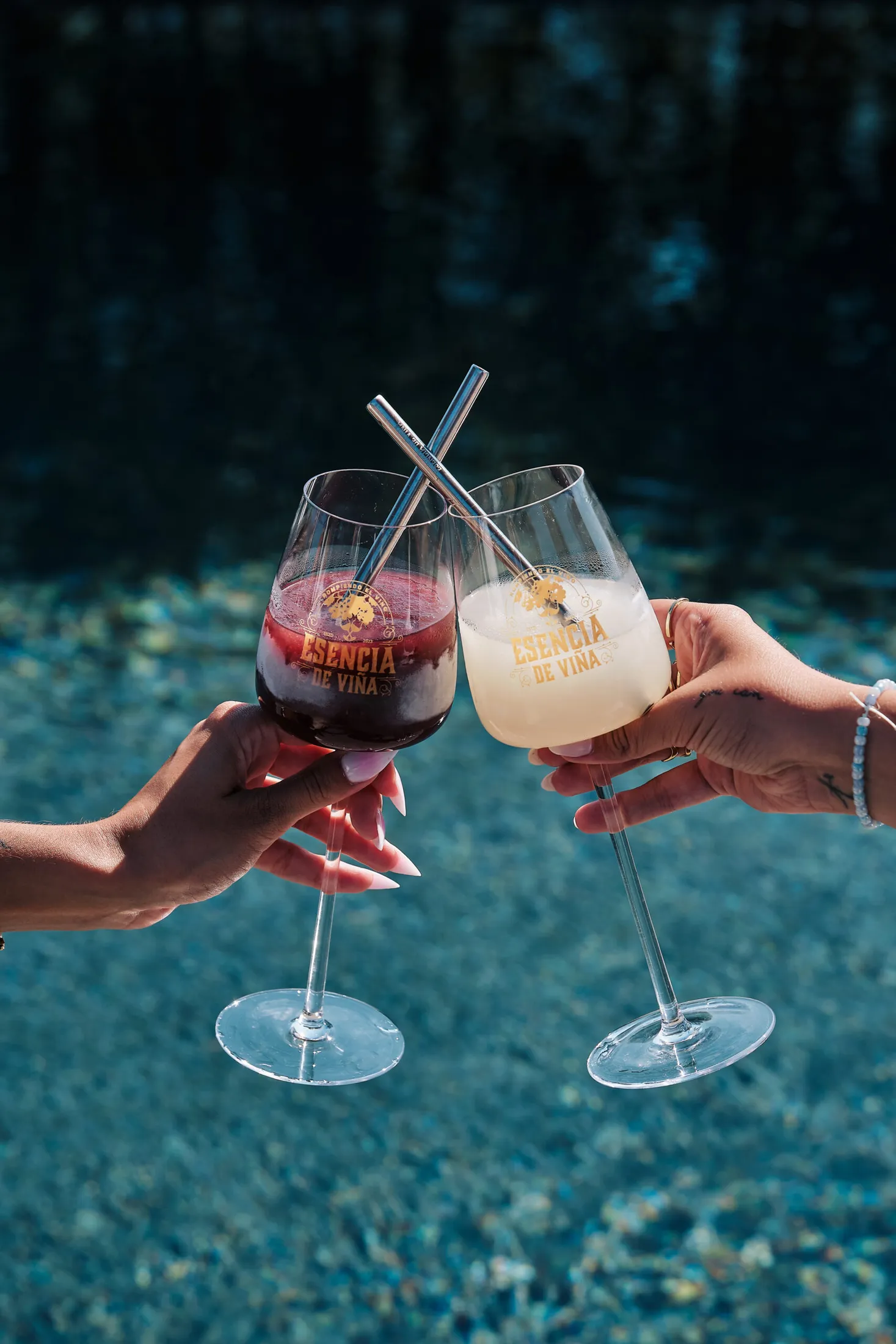 Dos manos brindan con blanco y tinto sobre una piscina
